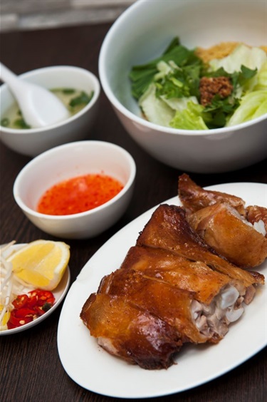 Plate of crispy chicken, big bowl of egg noodle with lettuce, small bowl of soup, fish sauce in a dipping sauce dish and small dish with lemon, chilli and bean sprouts