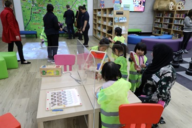 Group of young girls wearing high visibility vests playing with various wooden toys