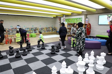 Guests and young children wearing high visibility vests walking past giant chess board