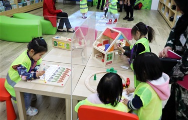 Group of young girls wearing high visibility vests playing with various wooden toys