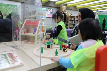 Group of young girls wearing high visibility vests playing with various wooden toys