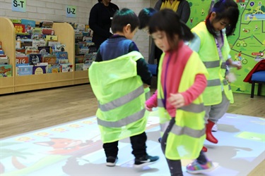 Group of young girls wearing high visibility vests playing with interactive floor projection