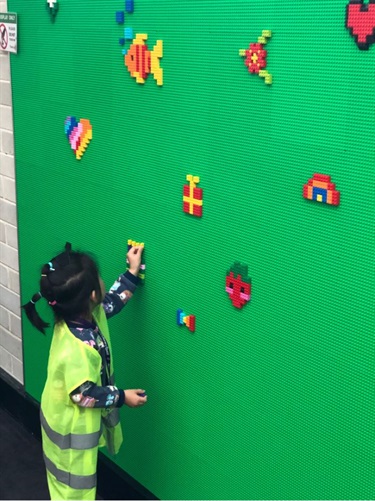 Young girl wearing high visibility vest placing building block onto Lego wall