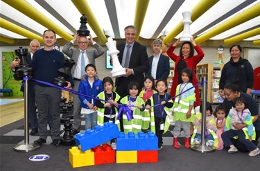 City Manager Alan Young, Councillor Adrian Wong, State Librarian John Vallance, Mayor Frank Carbone and Councillor Dai Le smiling and posing with giant chess pieces behind group of young children