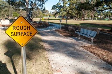 Sign saying Rough Surface near footpath and benches