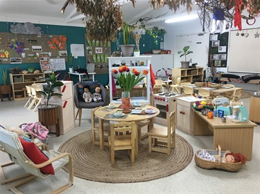 Crafts displayed on the walls, plants hanging from the ceiling, and toy kitchen appliances accompanied with toy food in the children's activities room