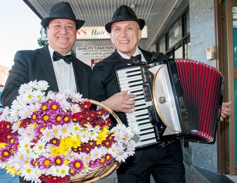 Men in black hats and suits playing accordion and holding up a basket of flowers