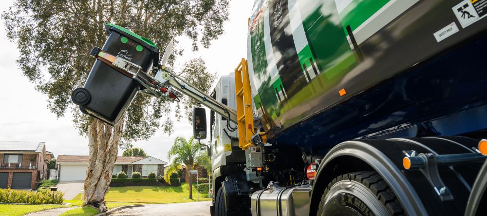 A garbage truck is collecting a green FOGO bin.