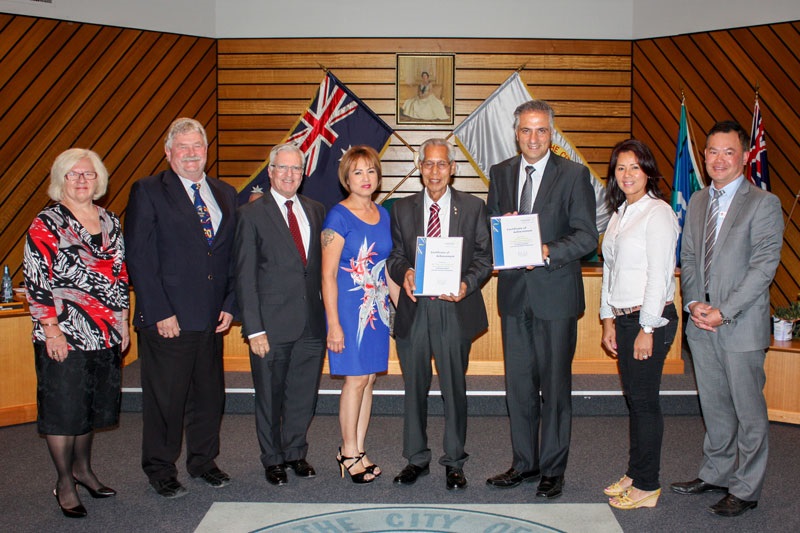 Mayor Frank Carbone and other officials smiling and posing with the Lim family, while presenting them with a certificate