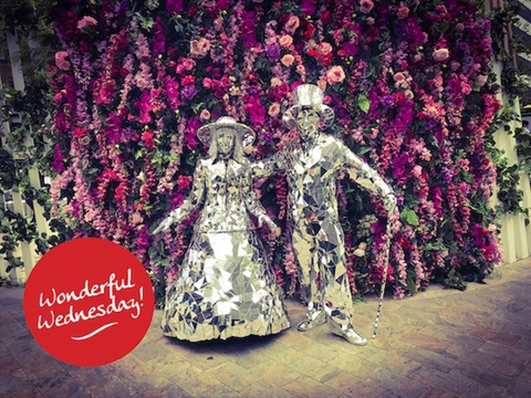 Statues of Man and Lady made from mirrors posing in front of a floral wall 