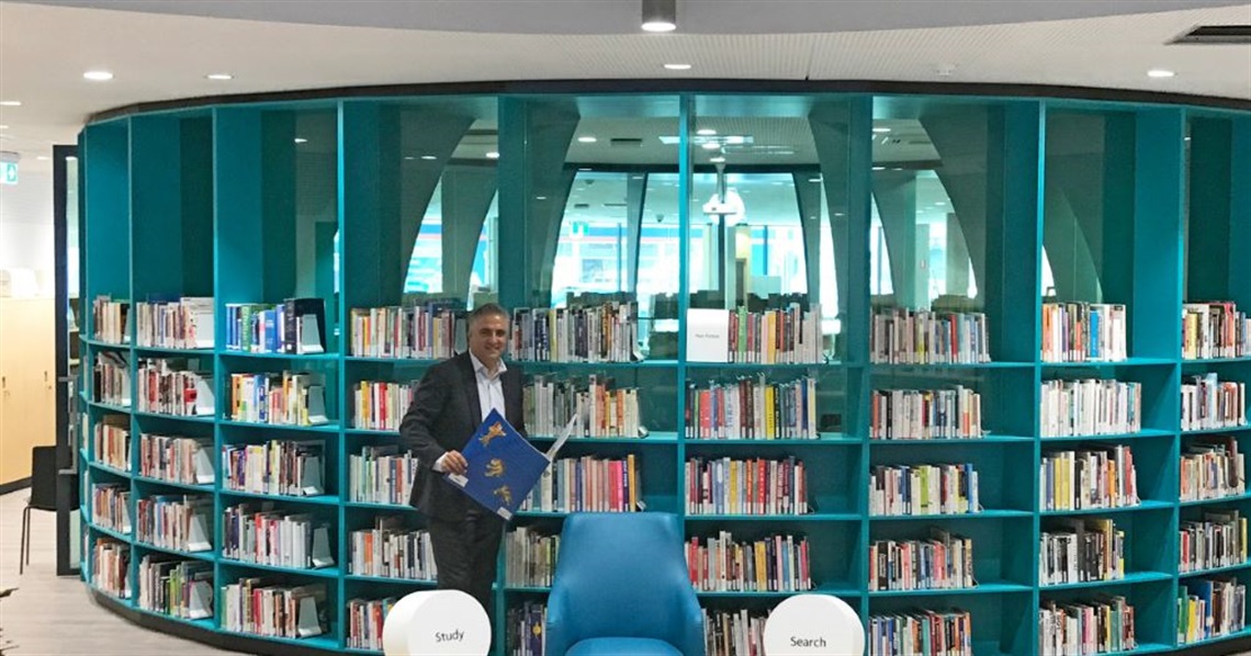 Mayor Frank Carbone smiling and posing with children's story book in front of book shelf at the new Fairfield Library 