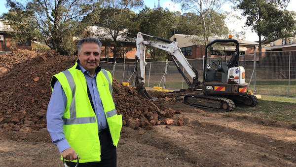 Mayor Frank Carbone, wearing a high visibility vest, smiling and posing at the construction site of Bossley Park Pre-School