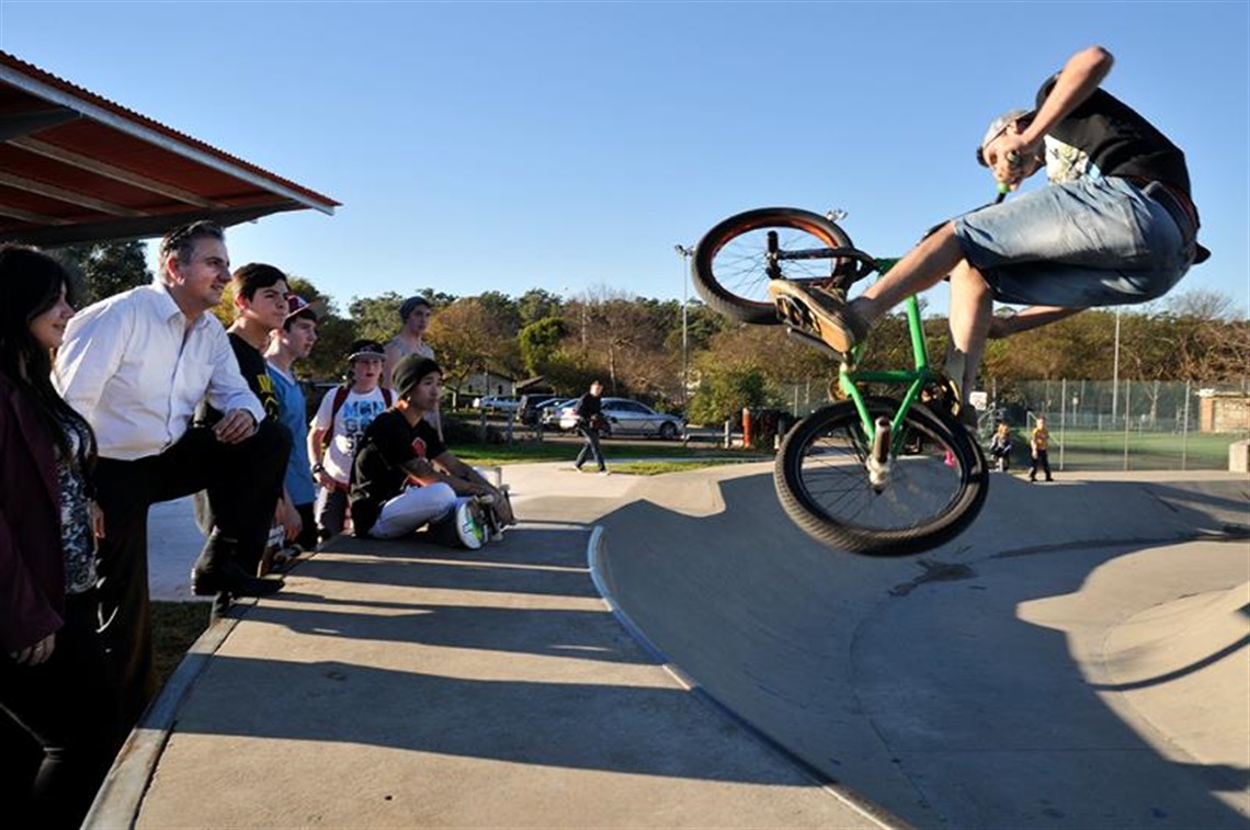 Mayor Frank Carbone smiling while watching young man doing bicycle tricks in the skate park bowl at Bonnyrigg Town Centre Park.